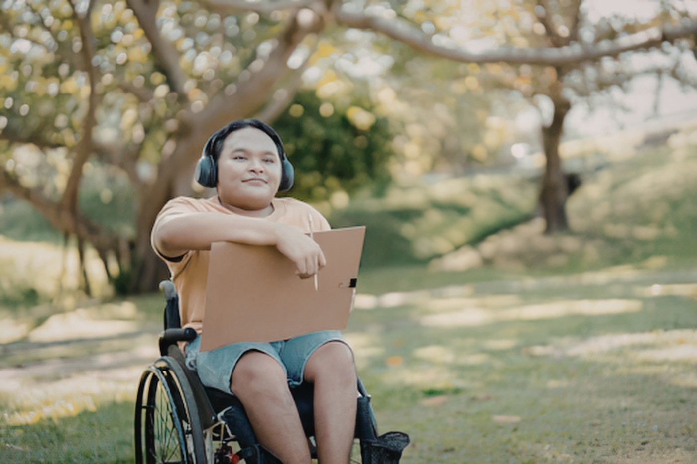 Young man in wheelchair using a laptop outdoors in a park