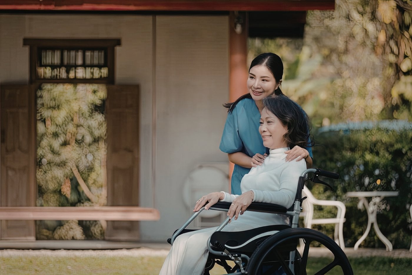 Carer pushing a woman in wheelchair outdoors near a house