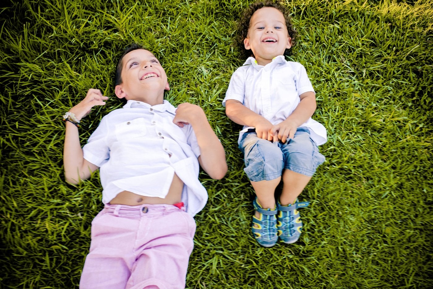 Two children laughing and lying on green grass in the sun