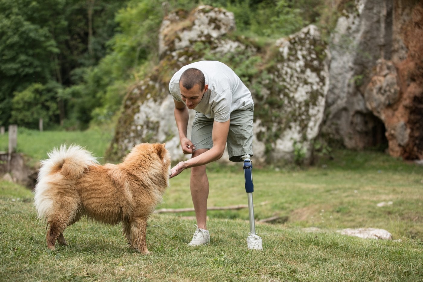 Man with prosthetic leg playing with his dog outdoors in nature