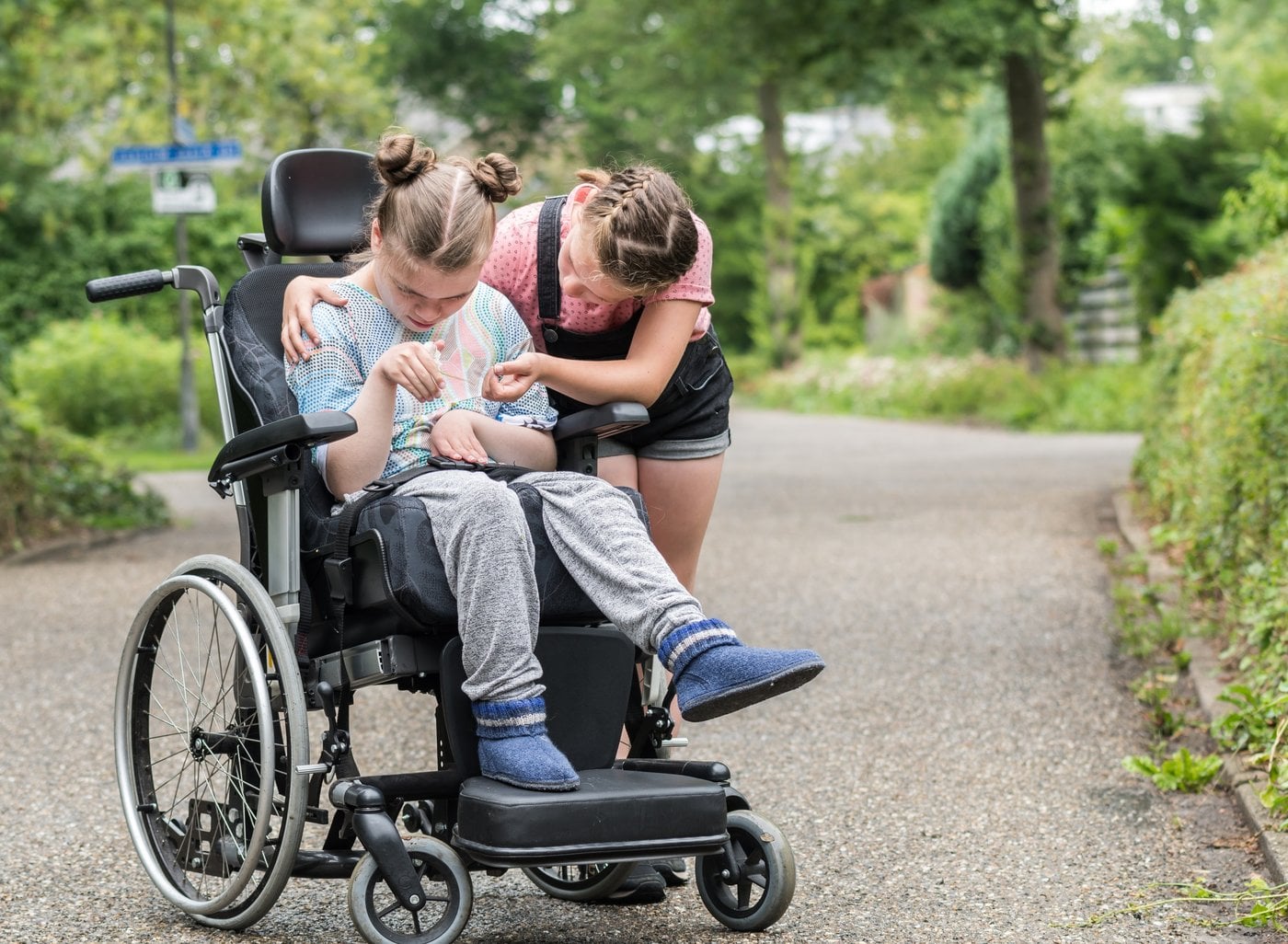 Girl helping her friend in wheelchair along a garden pathway