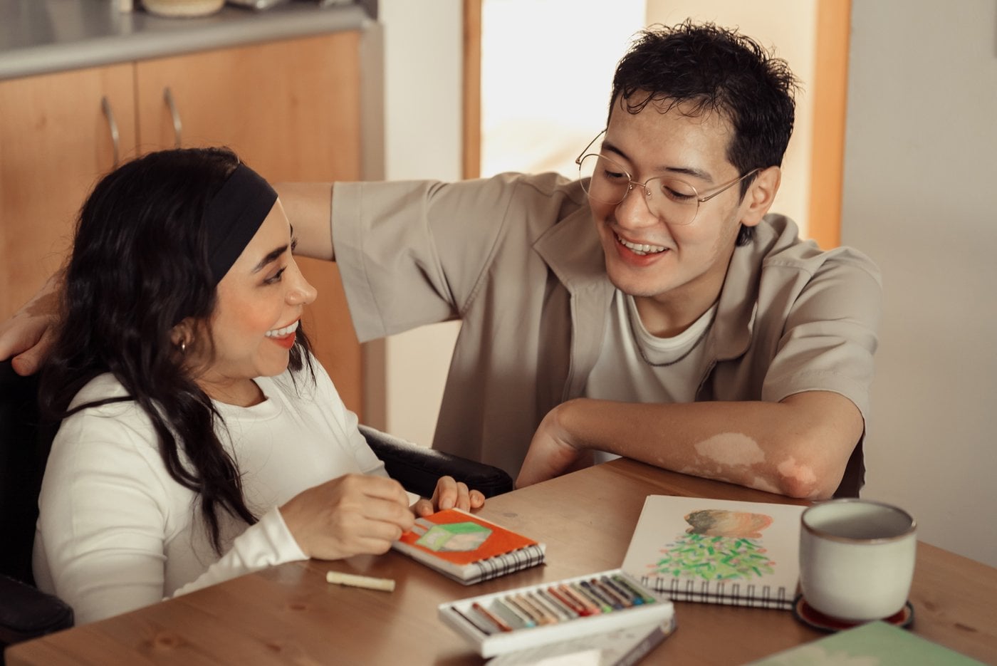 Two friends laughing while doing art together at a kitchen table