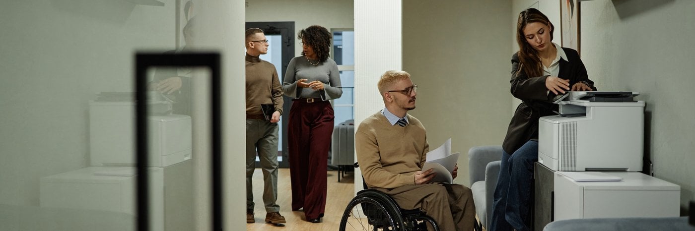 Inclusive office environment with wheelchair user working alongside colleagues