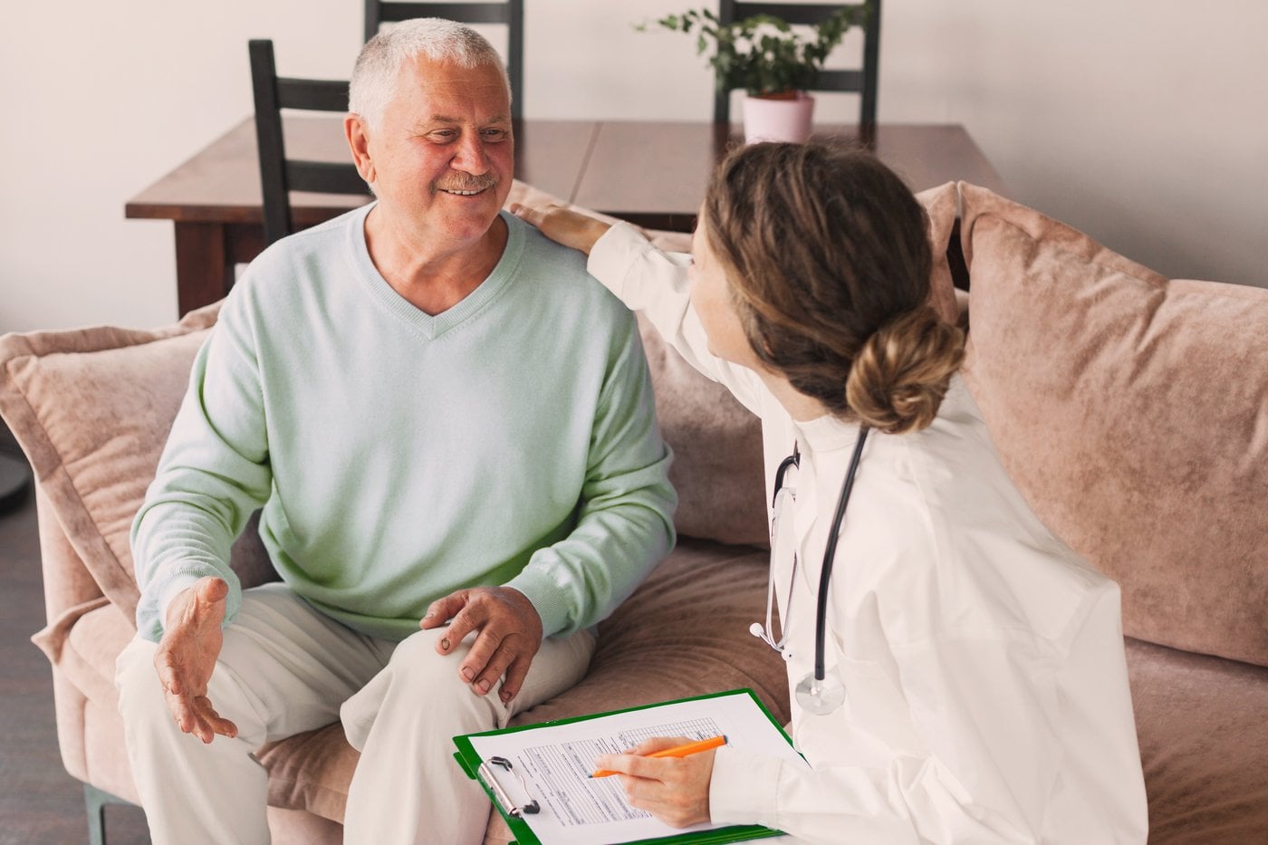 Nurse consulting an elderly man at home with clipboard and stethoscope